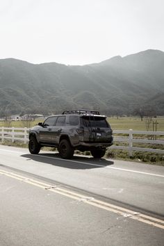 a jeep driving down the road in front of a white fence and mountains behind it