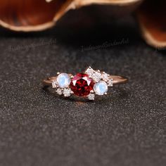 a red and white diamond ring sitting on top of a black table next to shells