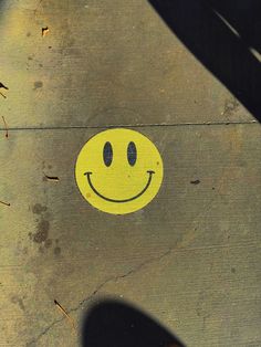 a yellow smiley face painted on the side of a sidewalk with someone's shadow