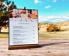 a menu sitting on top of a wooden table in front of a scenic field and trees