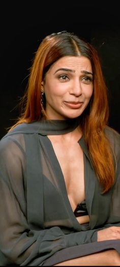 a woman with long red hair wearing a black shirt and posing in front of a dark background