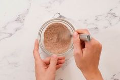 two hands are using a brush to apply some powder on the top of a jar