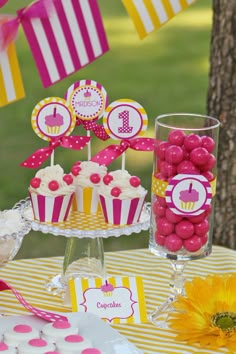 a table topped with cupcakes and candy on top of a yellow striped table cloth