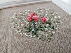 a close up of a cross stitched rug with red flowers on it and small white flowers in the middle