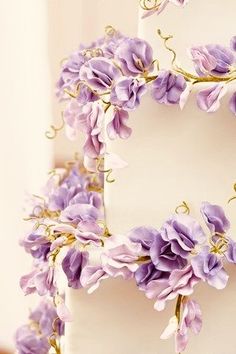 a white cake with purple flowers on top and green stems sticking out of the side