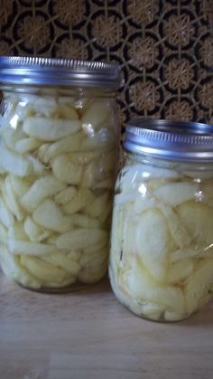 two jars filled with sliced apples sitting on top of a table