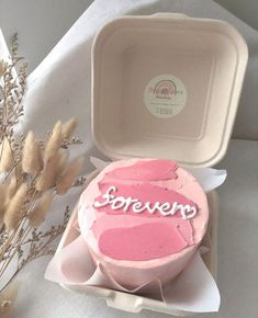 a pink cake with the word forever written on it in front of a white box