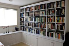 a large book shelf filled with lots of books next to a window in a room