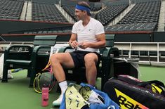 a tennis player sits on the bench with his racket and bag next to him