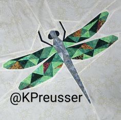 a close up of a quilt with a dragonfly on it's back and the words kreusser above it