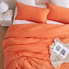 an orange comforter on a bed with white pillows and a photo frame next to it