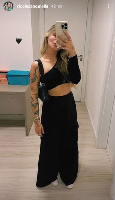 a woman taking a selfie with her cell phone in the mirror while wearing black pants