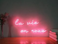 a pink neon sign that says la vie on rose next to a stack of books