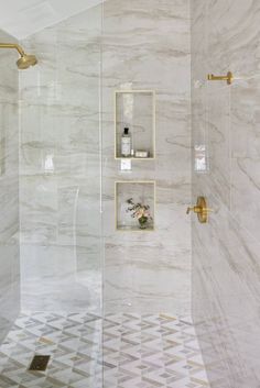 a bathroom with white marble walls and gold fixtures on the shower wall, along with a tiled floor