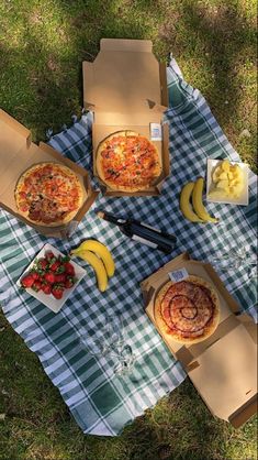 three pizzas are sitting on a picnic blanket with bananas and strawberries next to them