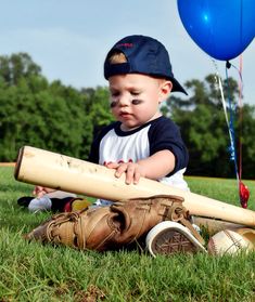 a young boy sitting in the grass with a baseball bat and ball next to him