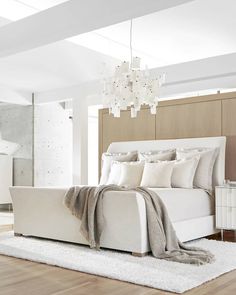 a white bed sitting on top of a wooden floor next to a wall mounted light