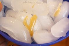 ice cubes and lemon juice in a blue bowl with someone holding an orange slice