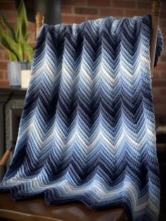 a blue and white crocheted blanket sitting on top of a wooden chair next to a brick wall