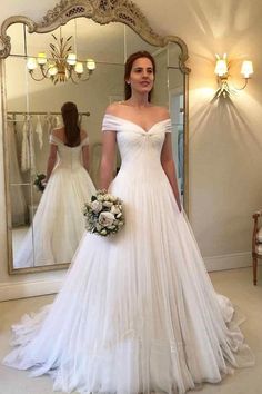 a woman is standing in front of a mirror wearing a wedding dress with off the shoulder sleeves