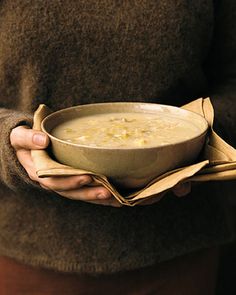 a person is holding a bowl of soup in their left hand while wearing a brown sweater