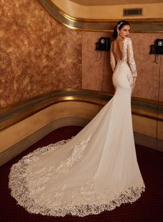 a woman in a wedding dress standing against a wall with her back to the camera