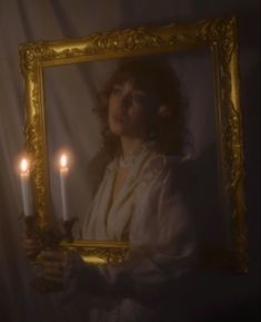 a woman holding two candles in front of a mirror