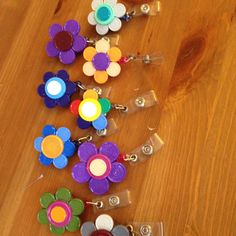 several different colored flower shaped badges on a wooden table with one being used as a keychain