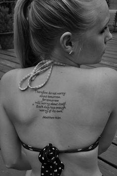 the back of a woman's neck with a quote tattooed on her upper part