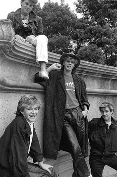 four young men sitting on the edge of a stone wall, posing for a photo