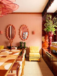 a dining room with yellow chairs and pink wallpaper, two mirrors on the wall