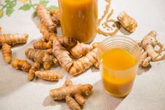 an orange juice in a glass next to some ginger root pieces on a tablecloth