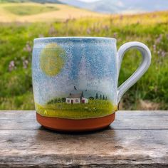 a coffee cup with a landscape painted on the outside and inside is sitting on a wooden table