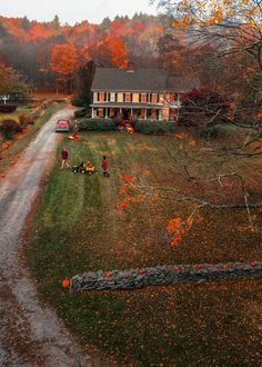 a house in the middle of a field with fall foliage around it and people standing outside