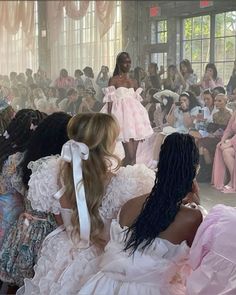 two women sitting in front of a large group of people wearing dresses with bows on their heads