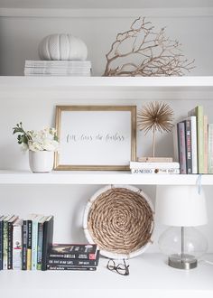 a white shelf with books, vases and other items on it in front of a framed sign