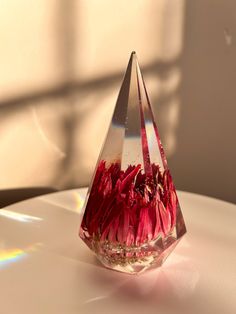 a glass vase filled with red flowers sitting on top of a white table next to a window