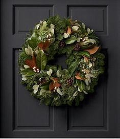 a wreath on the front door of a house that is decorated with greenery and pine cones