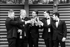 four men in tuxedos are toasting each other