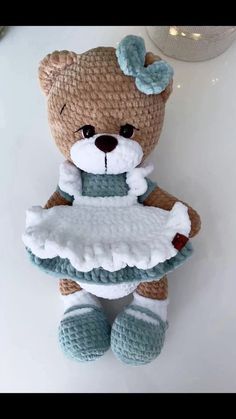 a crocheted teddy bear holding a dress on it's chest, sitting on a table