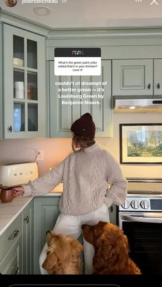 a woman standing in a kitchen with two dogs looking at something on the counter top