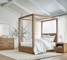 a bedroom with white walls and wood furniture, including a four poster bed frame in the middle