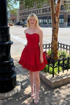 a woman in a short red dress standing on the sidewalk next to a lamp post