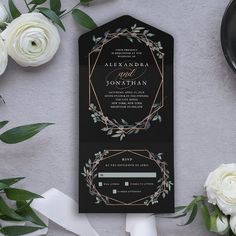 a black and white wedding card with greenery on it, next to some flowers