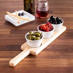 three small bowls filled with olives and pickles on a wooden tray next to a bottle of wine