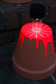 a red and black object with dripping paint on it's base, sitting on the ground