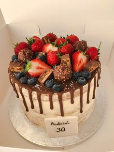 a white cake with chocolate and strawberries on top, in a box for sale