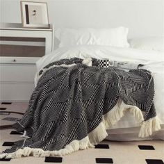 a black and white blanket on top of a bed next to a nightstand with drawers