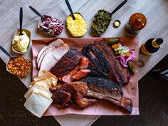 a table topped with meat and sides on top of a pink paper plate covered in condiments