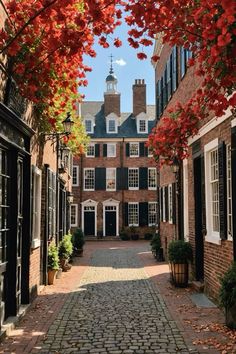 a cobblestone street lined with brick buildings and red leaves on the trees in front of them